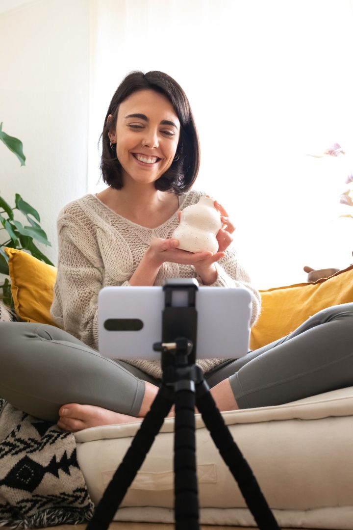 Woman DIY influencer shows handmade artisan ceramic vase at camera recording online video. Vertical.